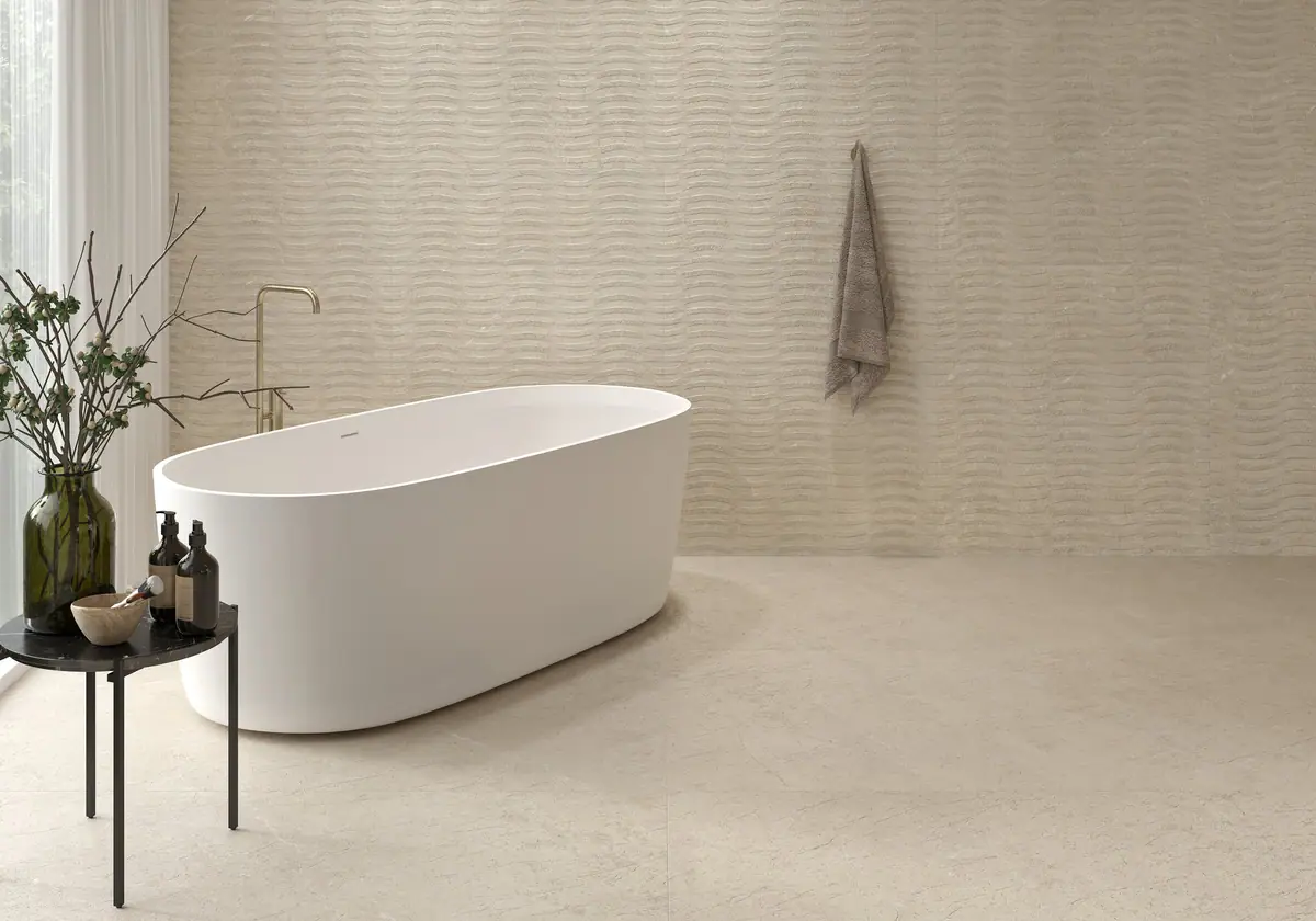 Bathroom with a white freestanding bath, a wall with a wavy relief and a light-toned stone-effect porcelain floor