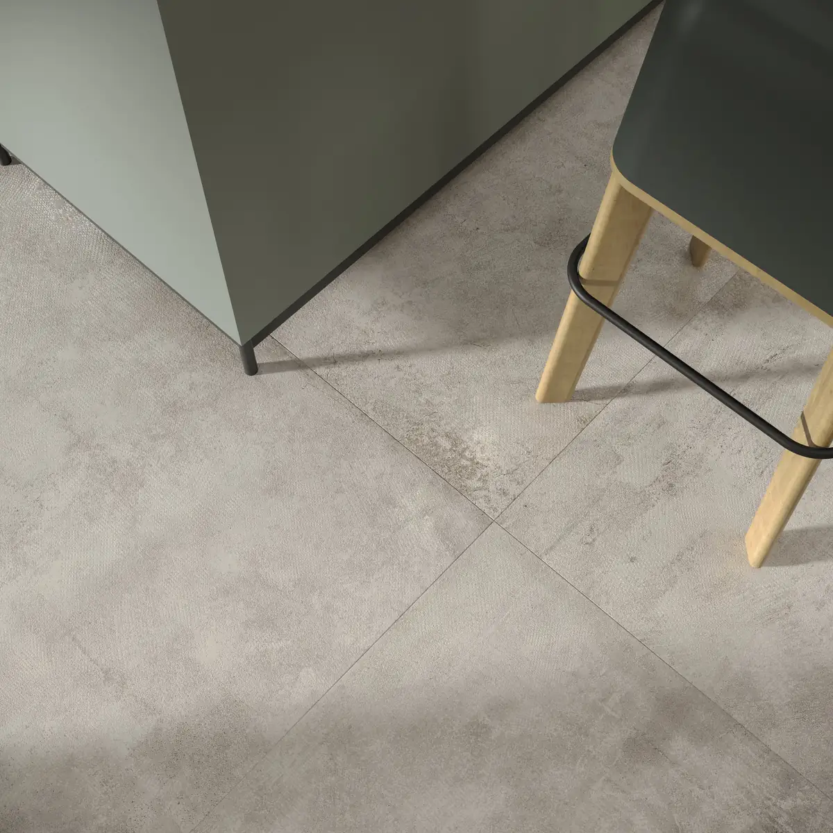 Large-format grey cement-effect porcelain floor beneath a kitchen unit and a wooden stool