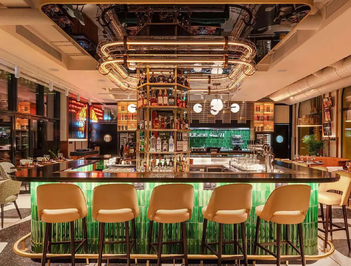 Bar counter with cream upholstered stools and an illuminated front of green tiles