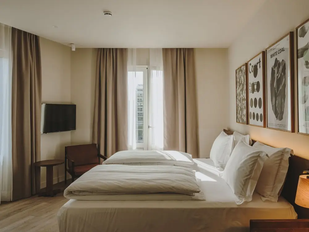 Hotel room with taupe curtains and white sheers, a double bed and framed prints