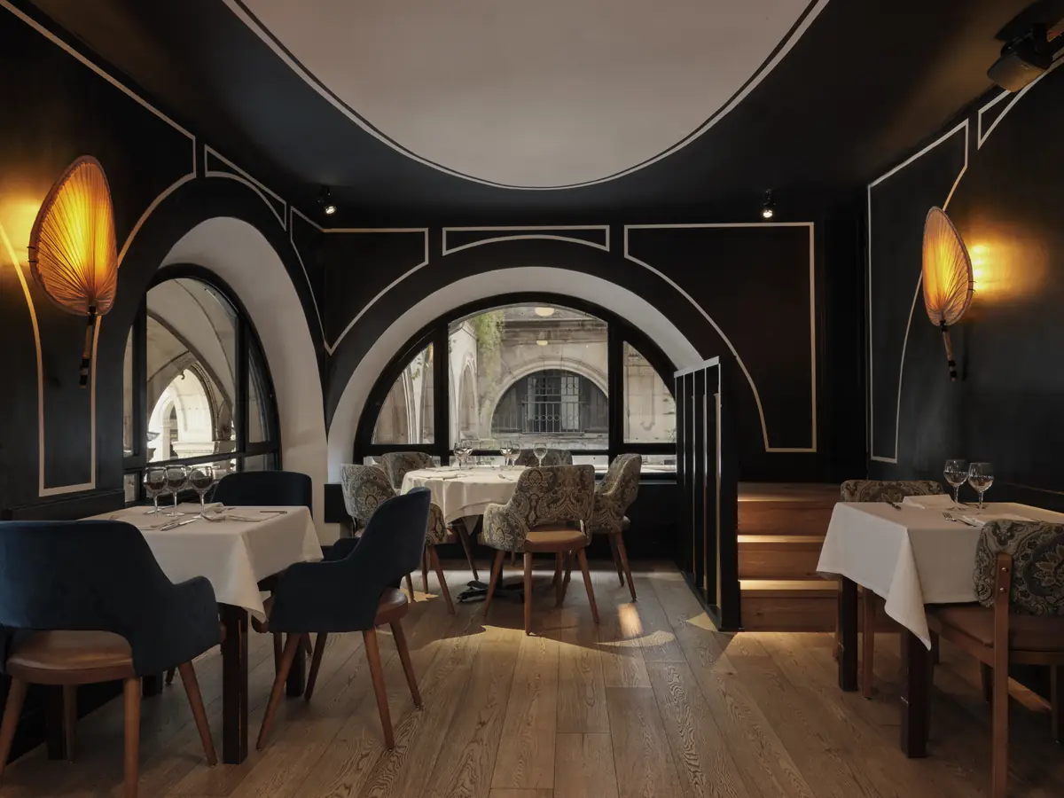 Dining room with black walls, white mouldings and arched windows, with chairs upholstered in blue velvet and in a paisley print