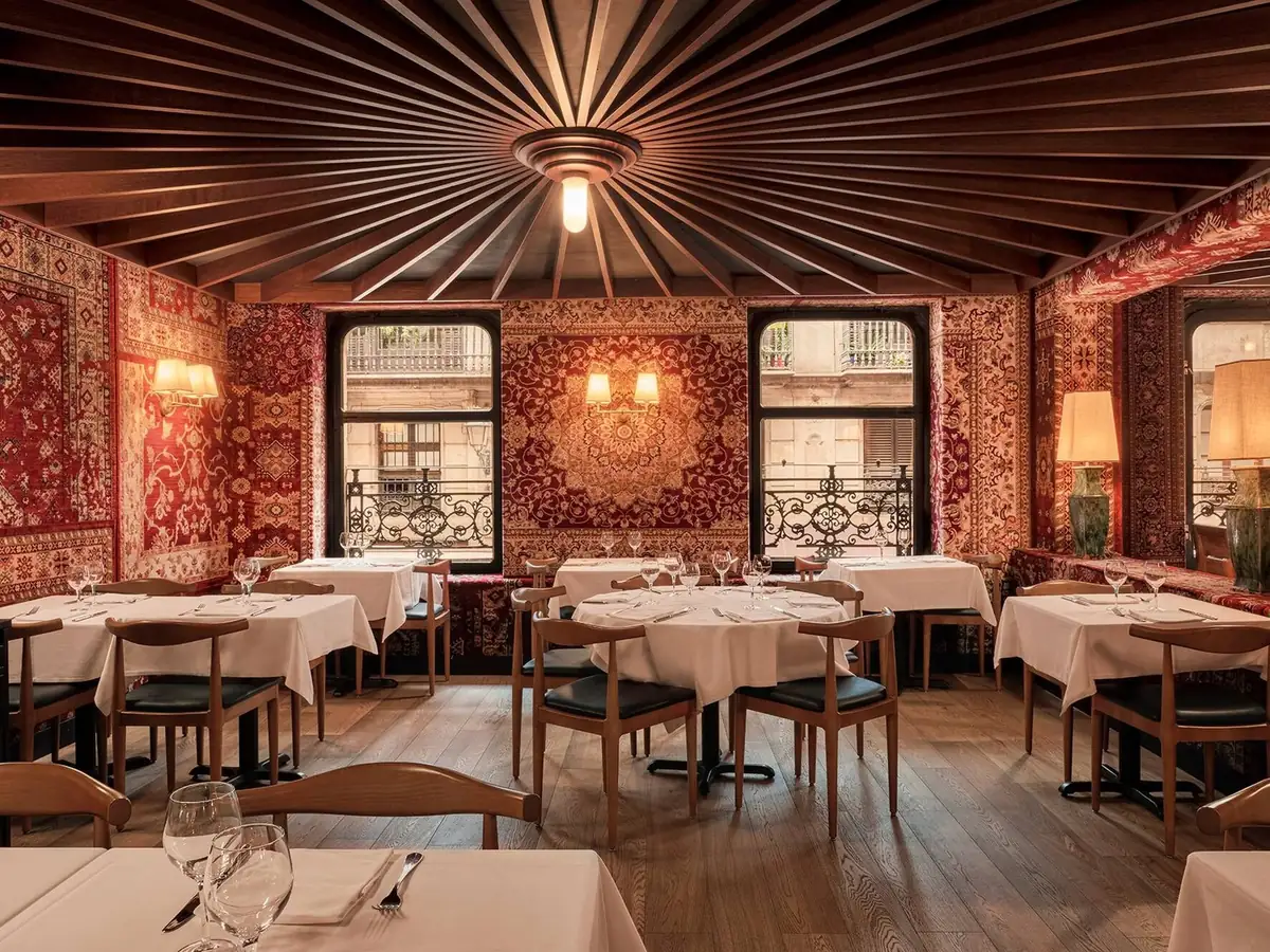 Dining room with walls and ceiling lined with red oriental rugs, a ceiling of radial slats and tables with white tablecloths