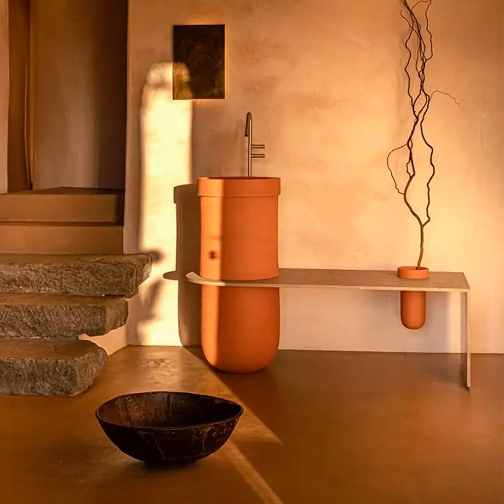Cylindrical terracotta ceramic washbasin with an aluminium bench extending from it and a small container holding dry branches