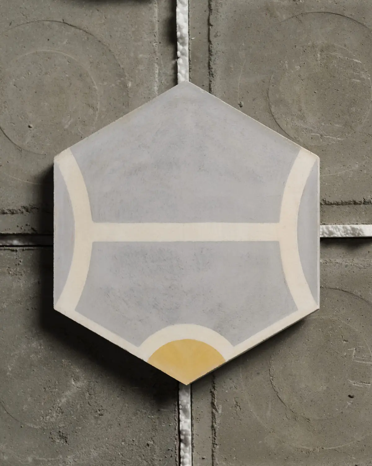 Hexagonal grey cementina tile with white lines and a yellow semicircle on a cement background