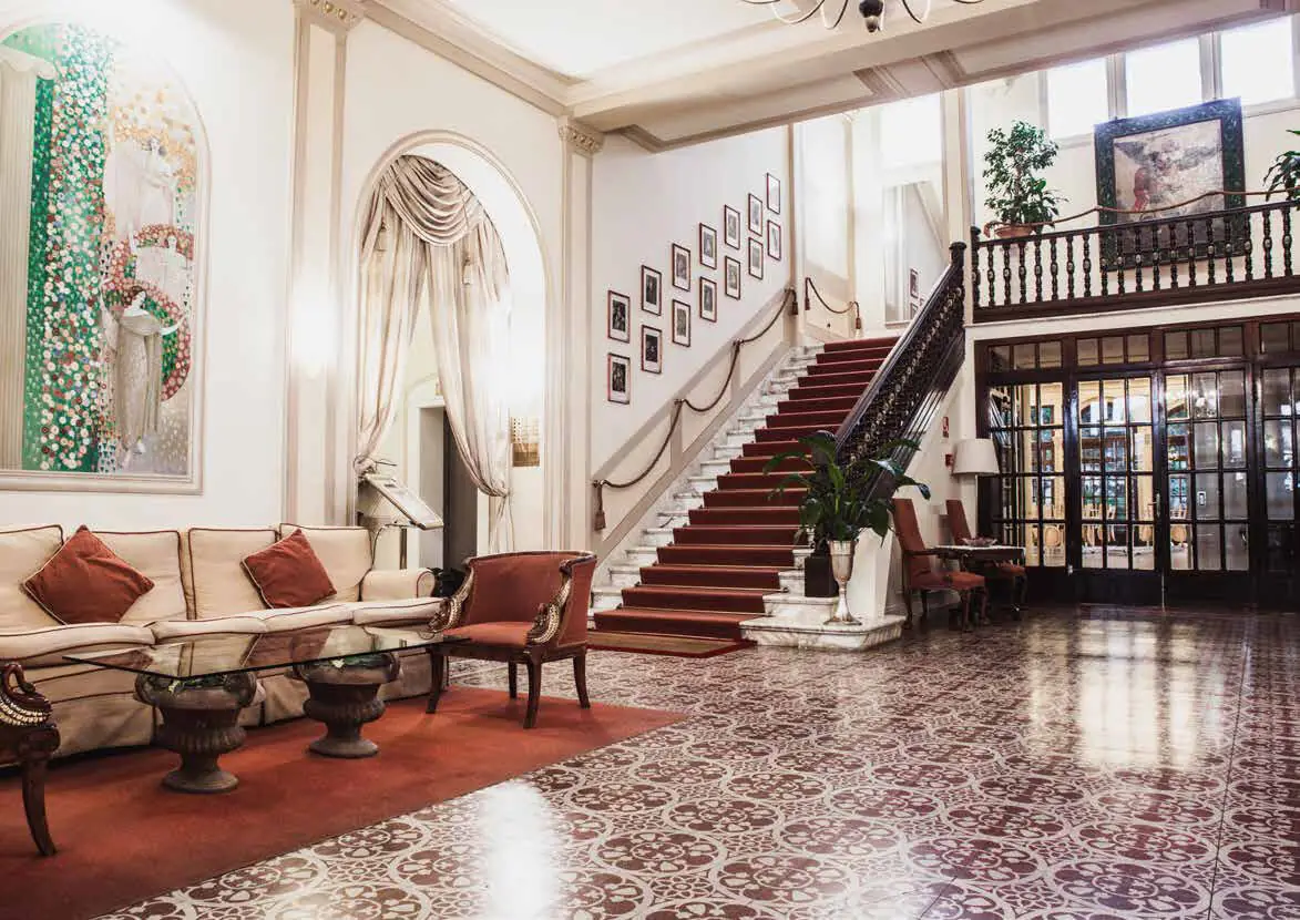 Hotel reception with a staircase, sofas and a floor of decorated burgundy and white tiles