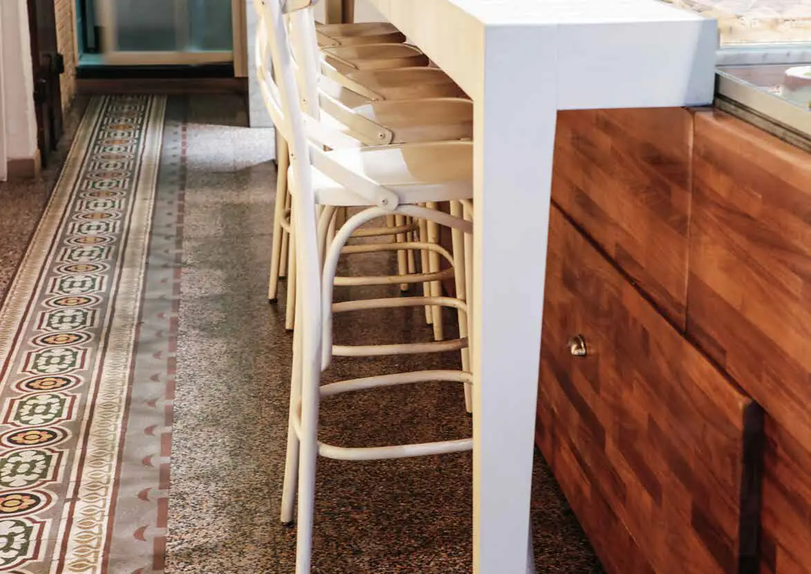 Graniglia floor with a decorated border next to a bar counter with white stools