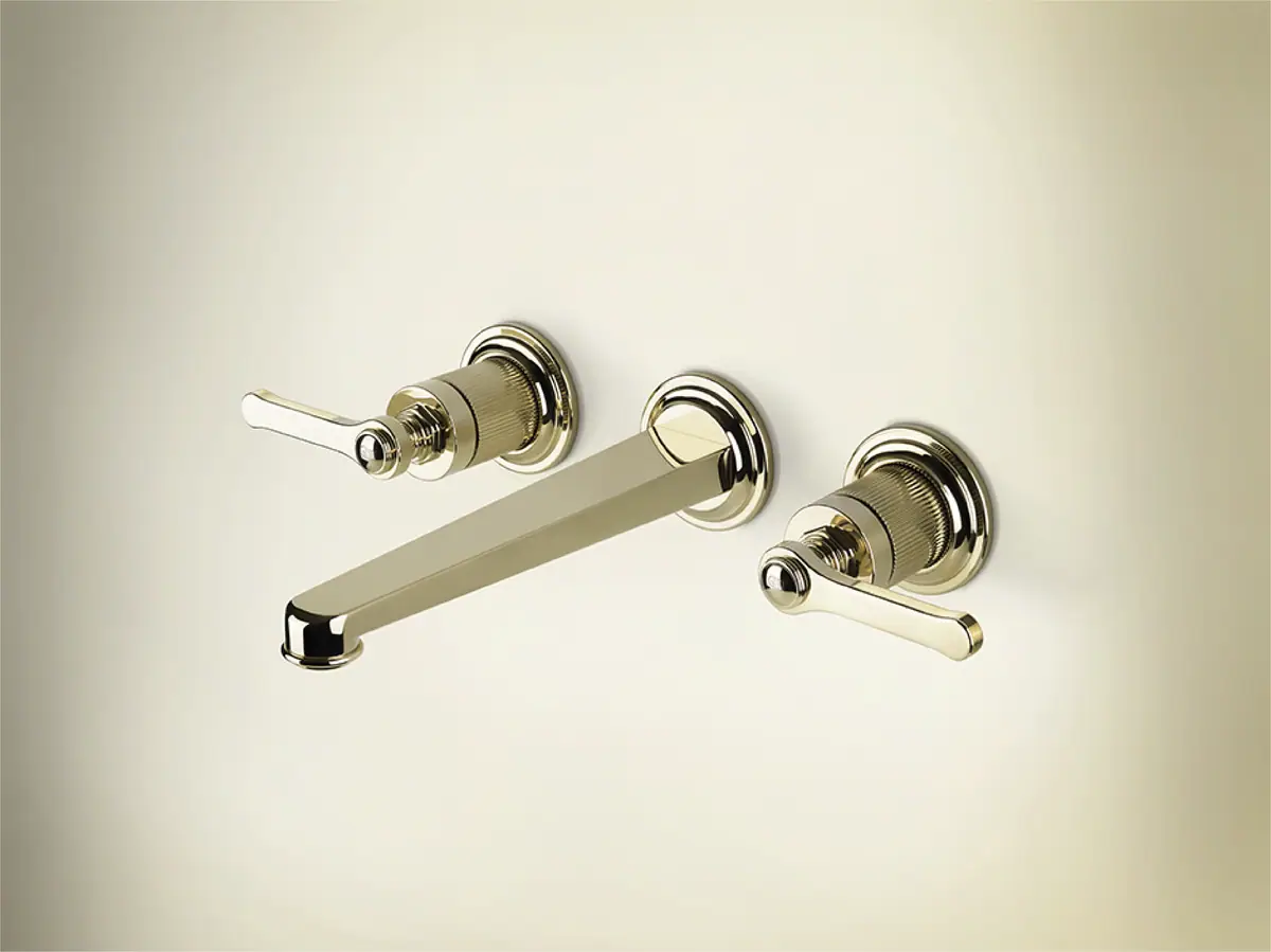 Three-piece wall-mounted basin tap with a long flat spout and two handles on stepped rosettes, in a bright gold metallic finish