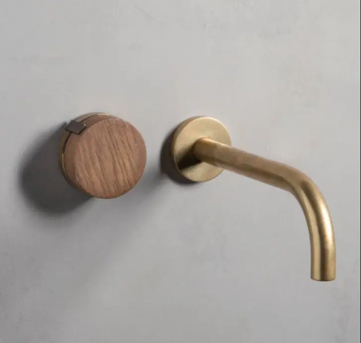 Wall-mounted basin tap with a curved brass spout and a round handle with a wooden cap on a grey wall