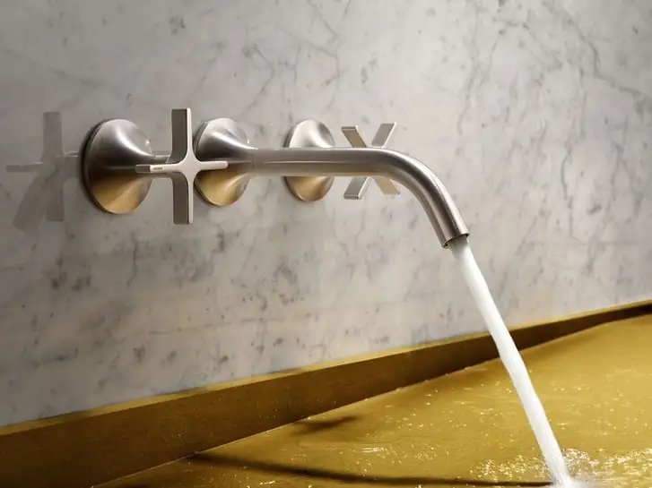 Wall-mounted tap with a long spout and two cross handles in a brushed metal finish on white marble