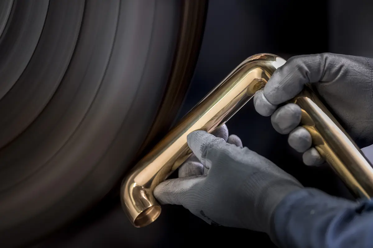 Gloved hands holding a polished brass tap spout next to a polishing wheel