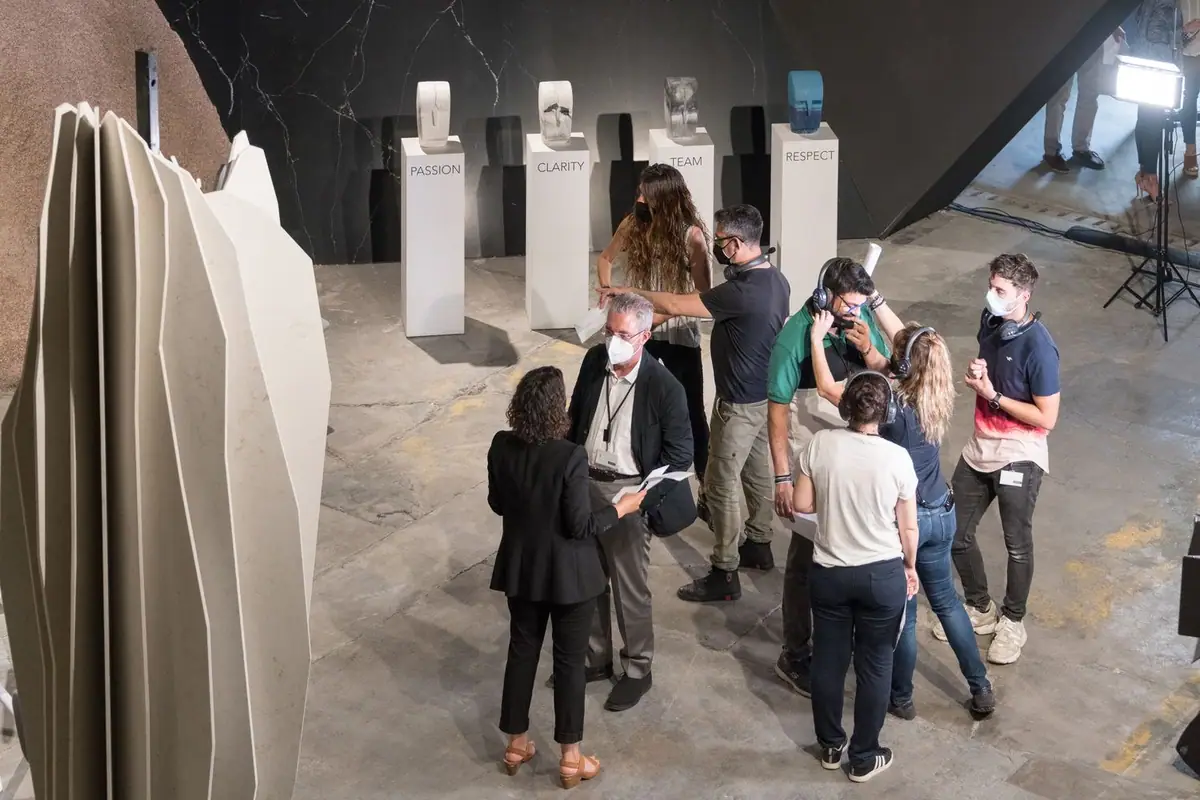 Members of the production team wearing headphones talk in front of four white plinths bearing the words Passion, Clarity, Team and Respect.