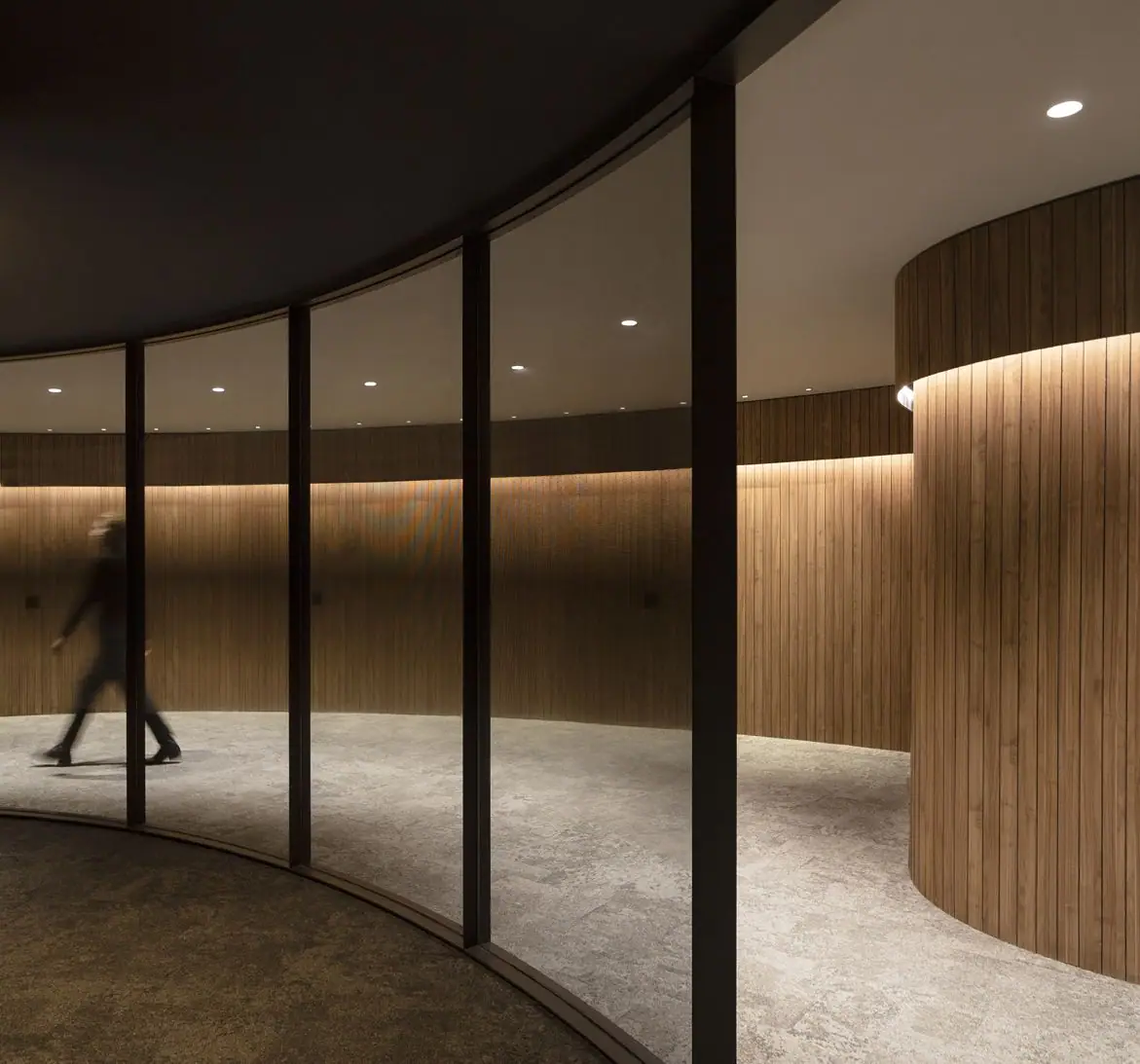 Curved corridor with a glazed front and walls clad in illuminated vertical timber slats