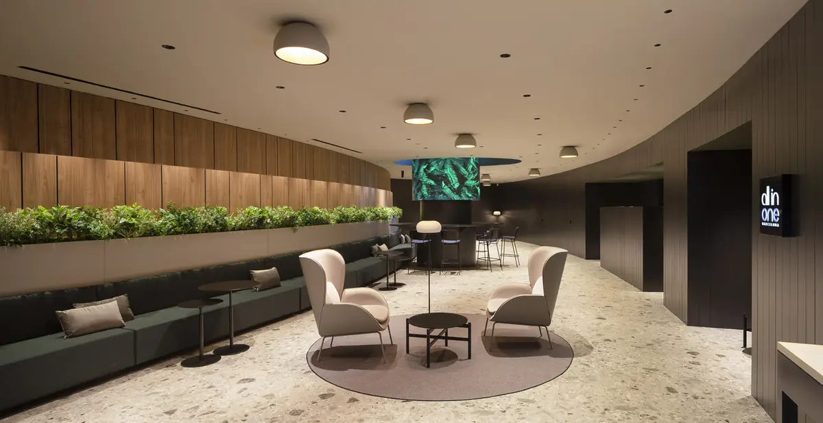Waiting area with a continuous green bench, a planter, light armchairs and timber slat cladding on a curved wall