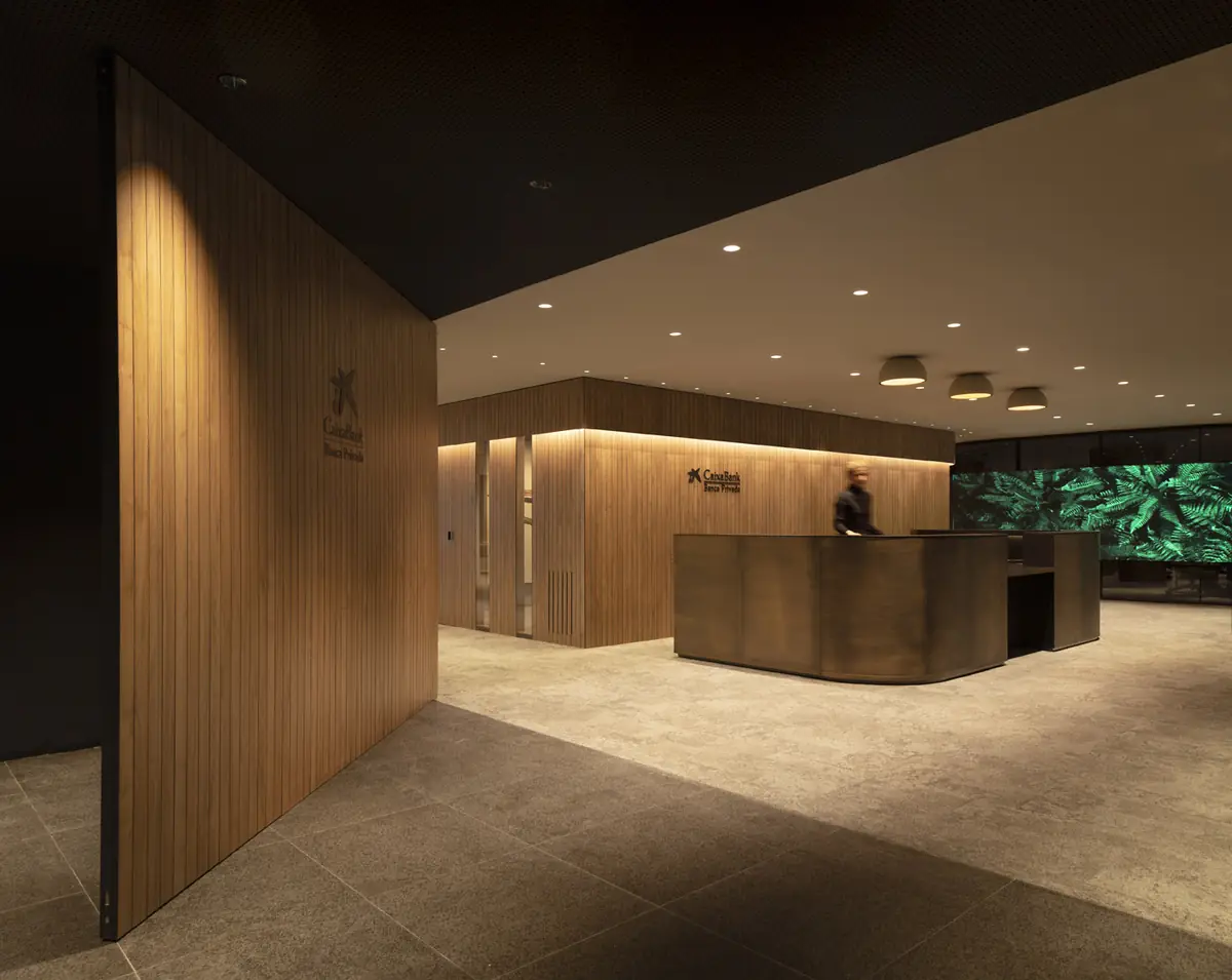 Banca Privada reception with a curved metal counter, timber slatted walls and a screen showing ferns in the background