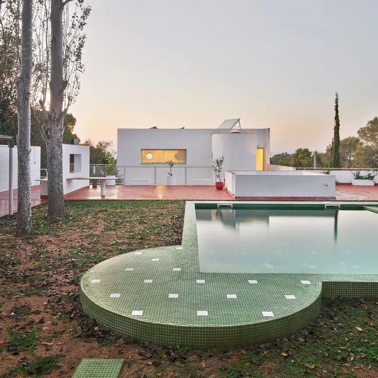 Fachada posterior blanca de Casa Hope al atardecer, con la piscina de gresite verde en el jardín