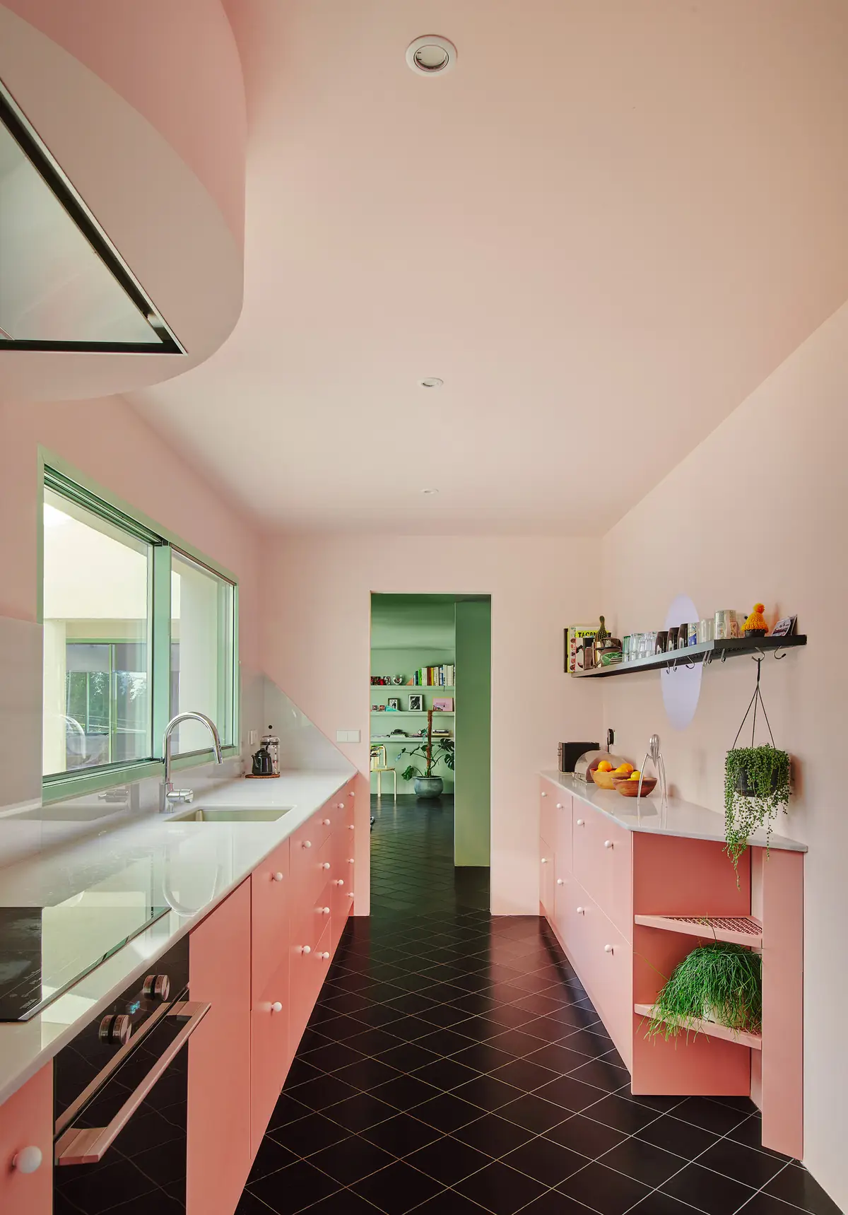 Cocina alargada con muebles rosa y pavimento cerámico negro colocado en diagonal