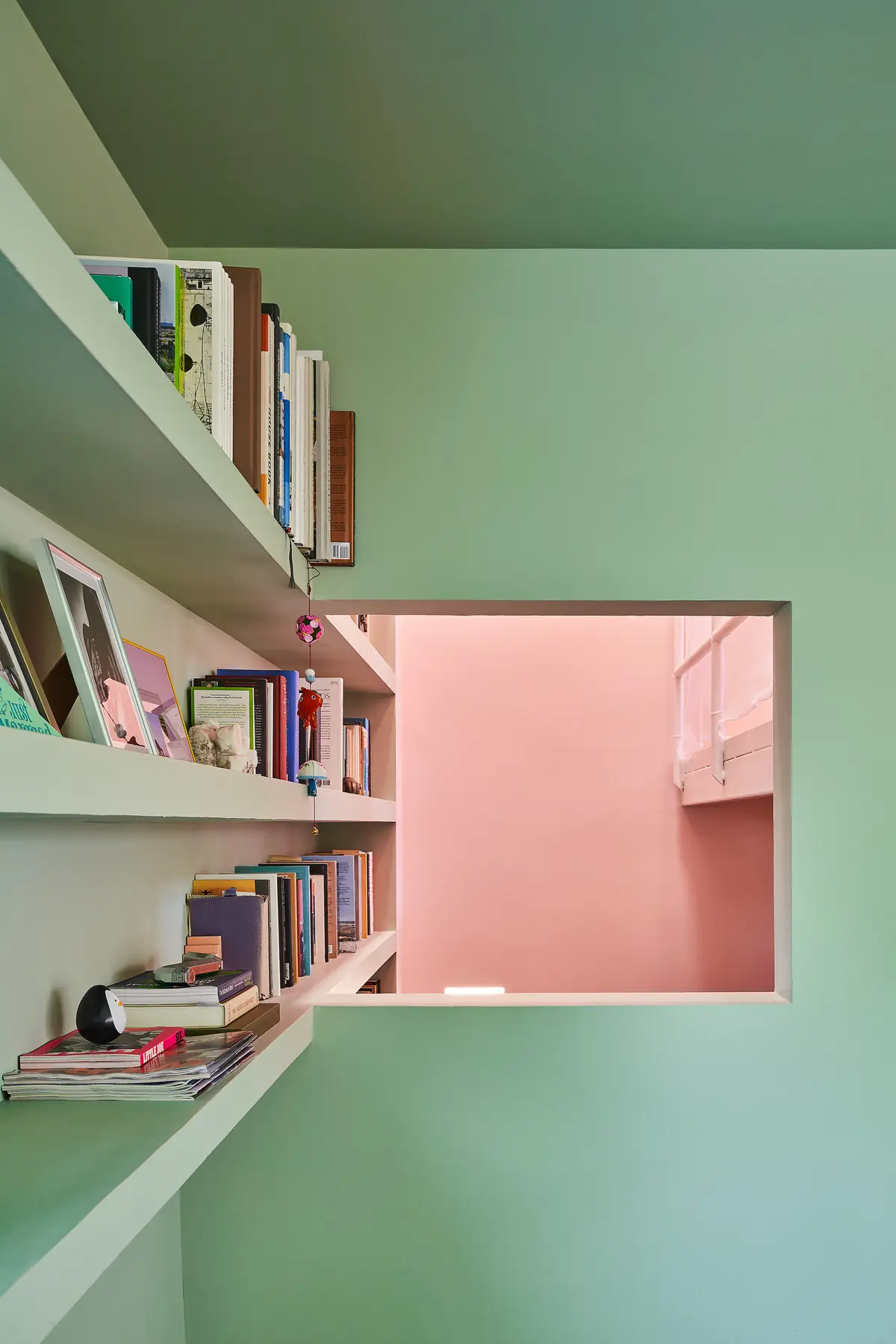 Abertura interior en una pared verde con estantes de libros que deja ver una estancia rosa