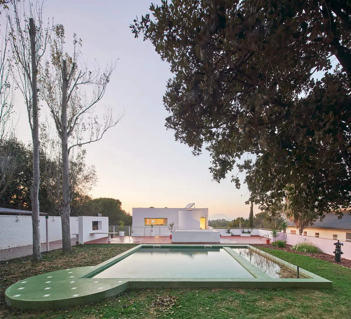 Piscina biológica rectangular con un círculo en una esquina, revestida de gresite verde, frente a la casa