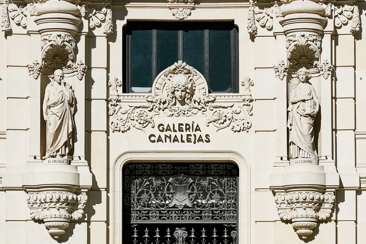 Portada de piedra de la Galería Canalejas con dos esculturas en hornacinas y puerta de hierro forjado
