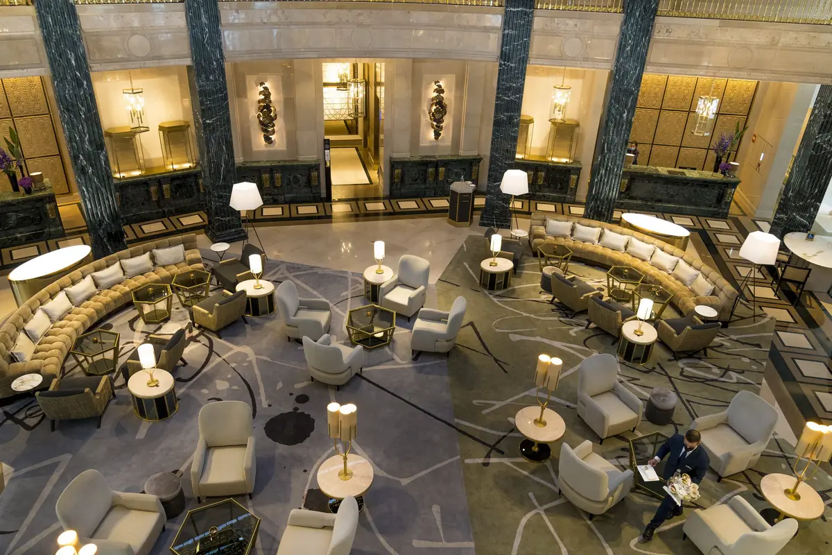 Vestíbulo del hotel con columnas de mármol oscuro, sofás curvos y lámparas de pie
