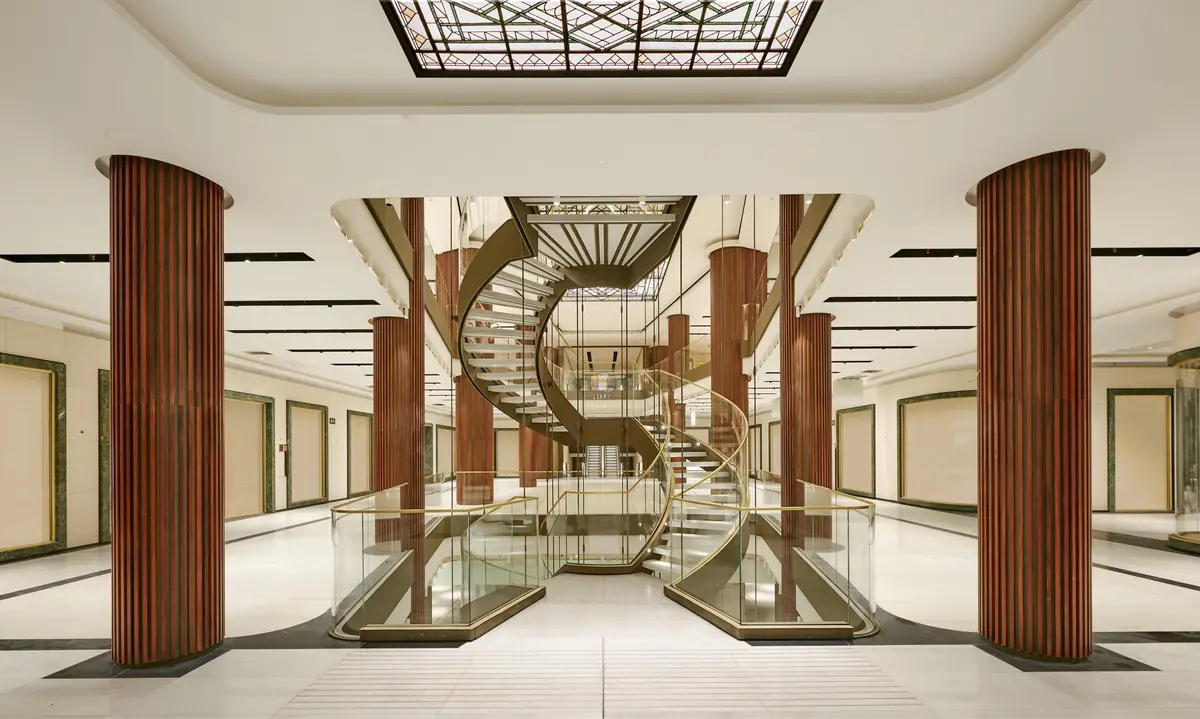 Interior de la galería comercial con columnas revestidas de madera y escalera helicoidal bajo un lucernario