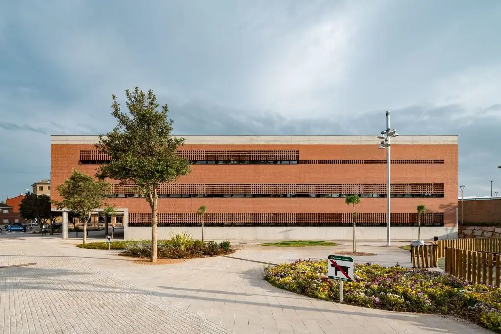 Long fair-faced brick facade with bands of ceramic latticework and the landscaped square in the foreground