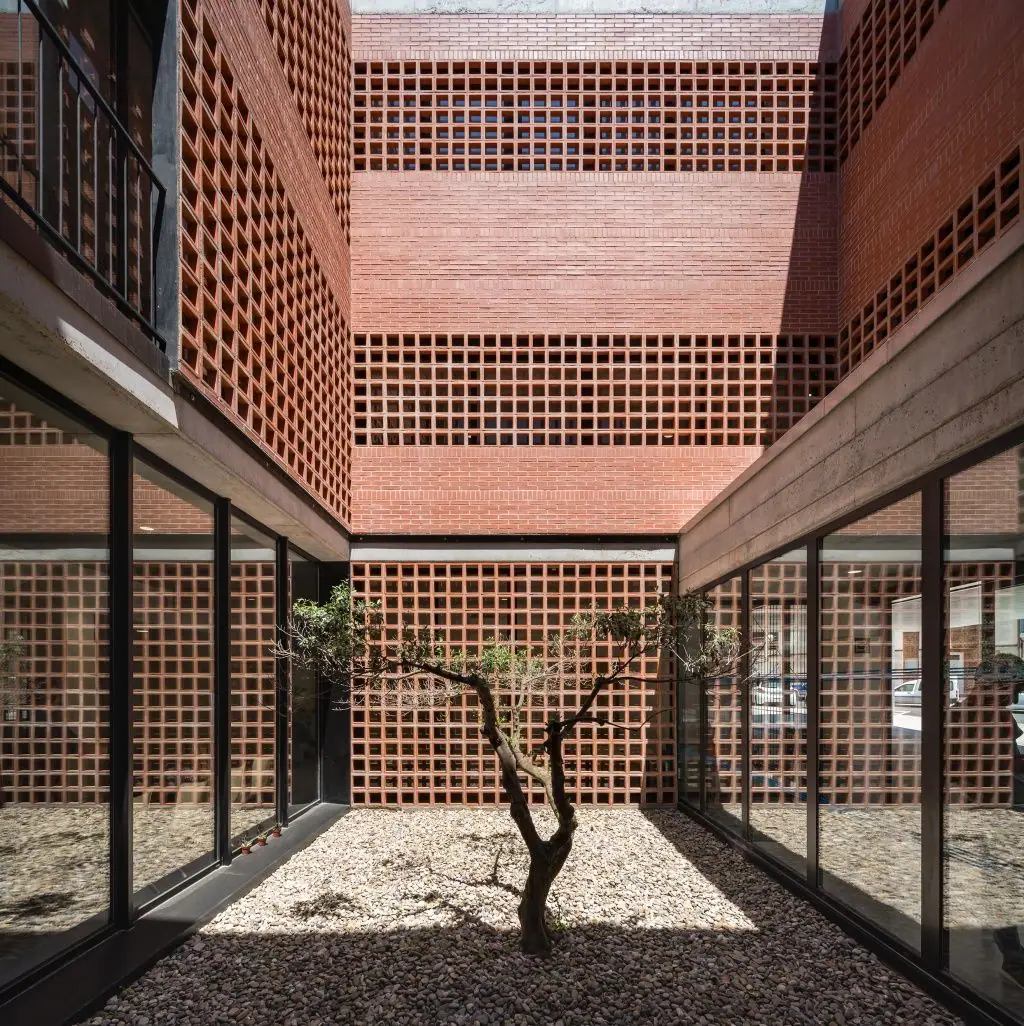 Interior courtyard with an olive tree on gravel, surrounded by brick walls and panels of ceramic latticework