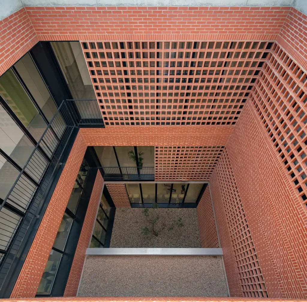 Overhead view of a courtyard with brick walls, panels of ceramic latticework and an olive tree at the bottom