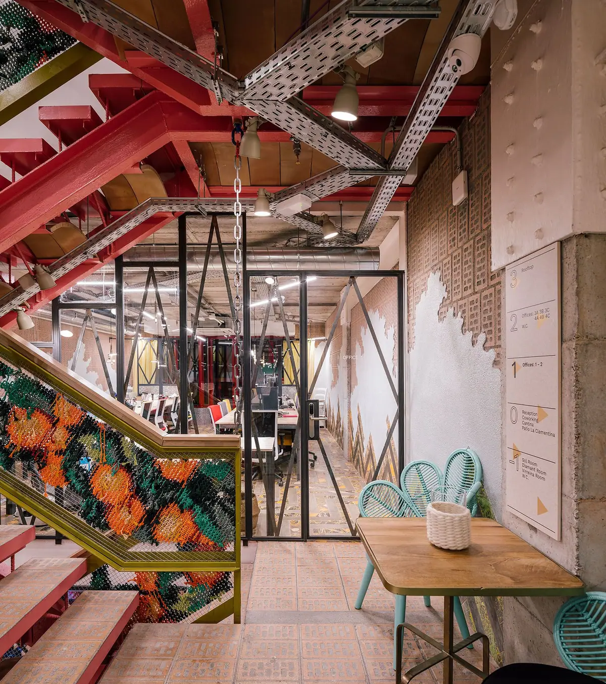 Red staircase with a mesh balustrade embroidered in orange and green threads, brick flooring and floor signage