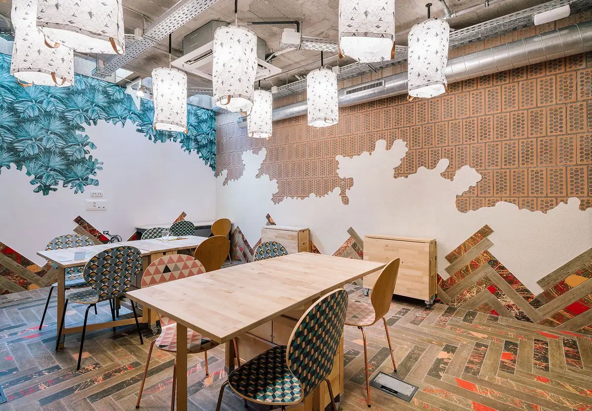 Meeting room with paper lamps, a leaf mural, exposed perforated brick and herringbone flooring splashed with colour