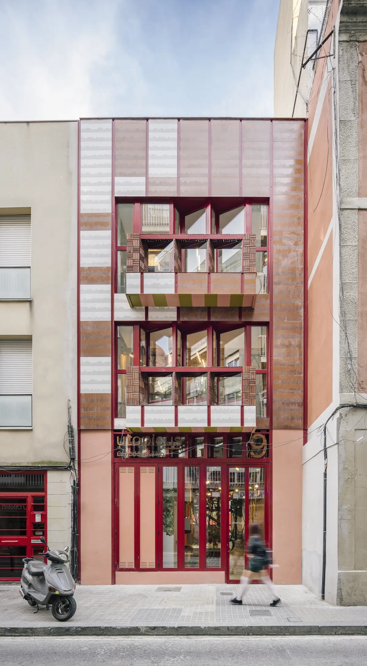 Street façade of Coworking Clementina, with ceramic pieces in terracotta and white tones and red window frames