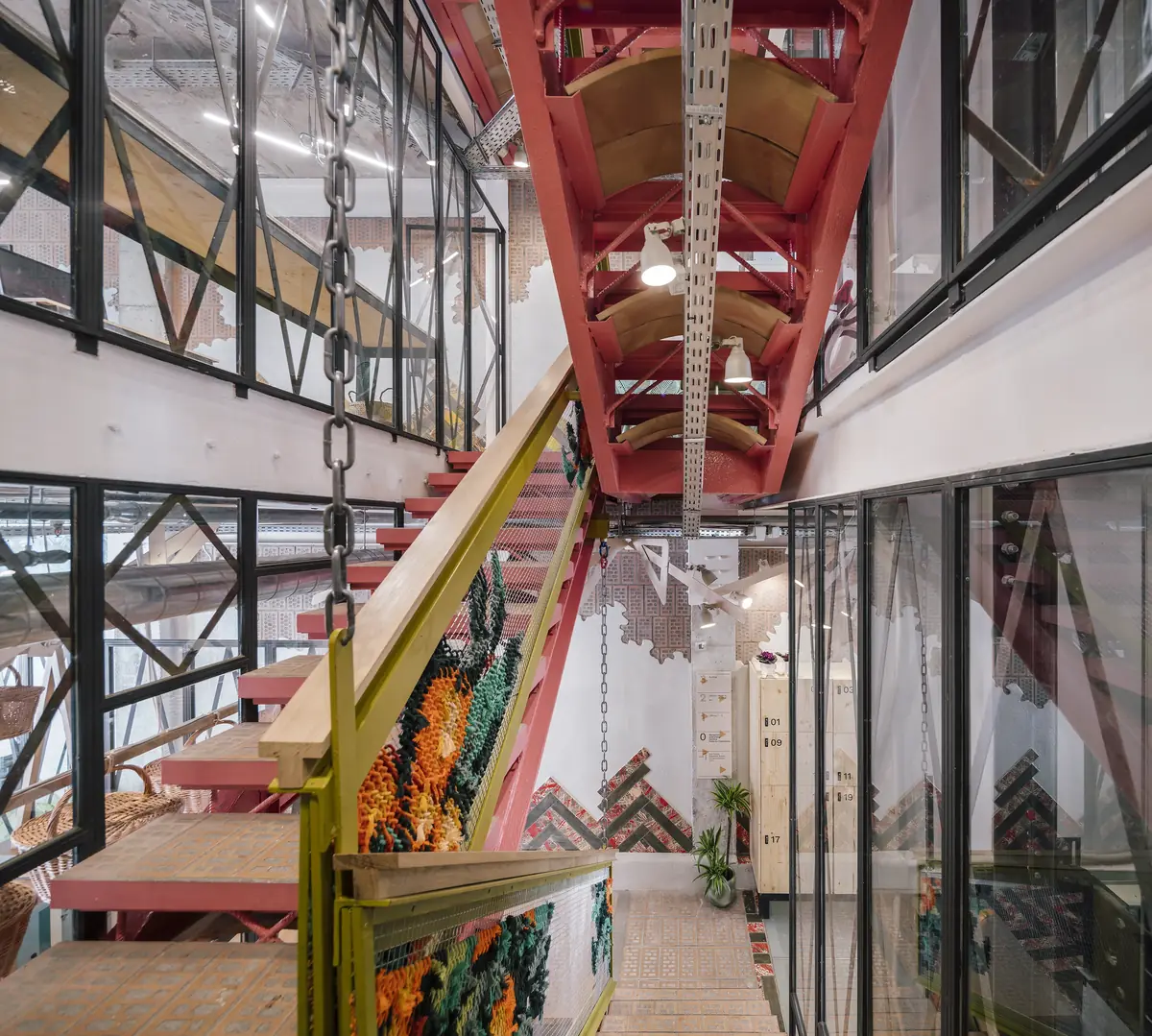 Central staircase with a red structure seen from below, between glazed rooms, with an embroidered balustrade