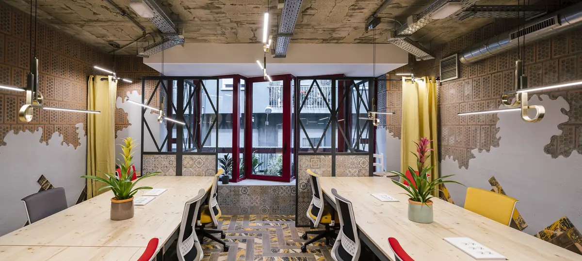 Workroom with shared wooden tables, office chairs, pendant lamps and exposed brick walls