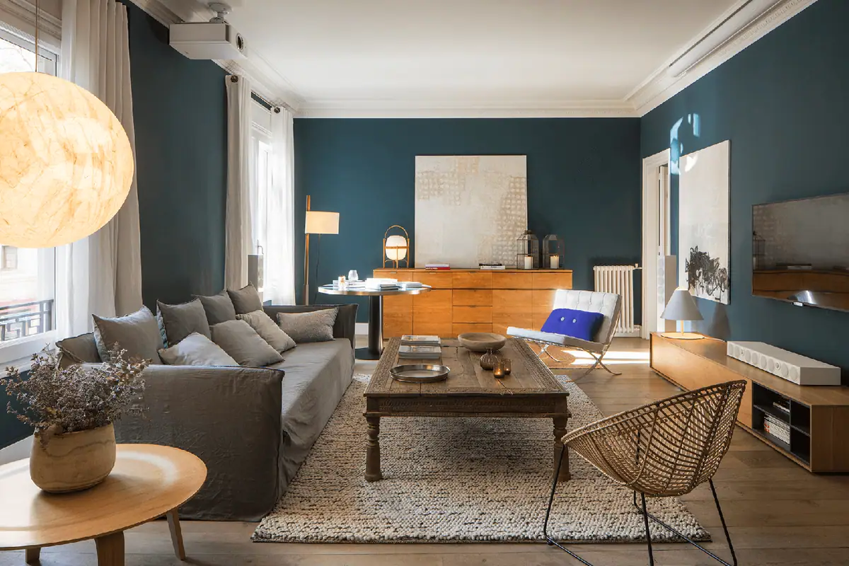 Salón con paredes azul oscuro, sofá gris, mesa de centro de madera y gran lámpara de papel