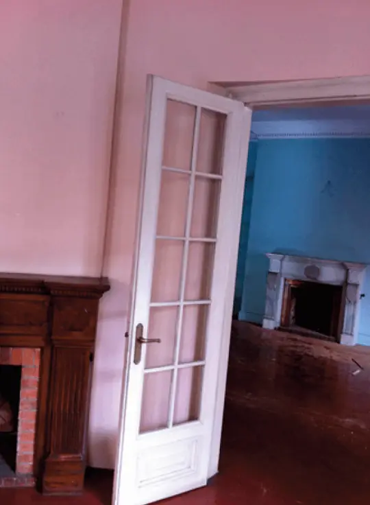 Estancia antes de la reforma, con paredes rosadas, chimenea de madera, puerta vidriera y una chimenea de mármol en la sala contigua