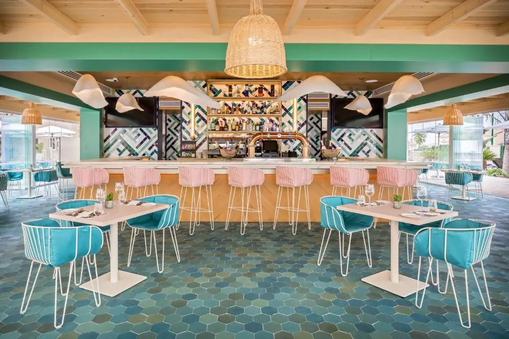 Gastrobar with a wooden bar, pink stools, turquoise chairs and a tiled front in blues, greens and whites