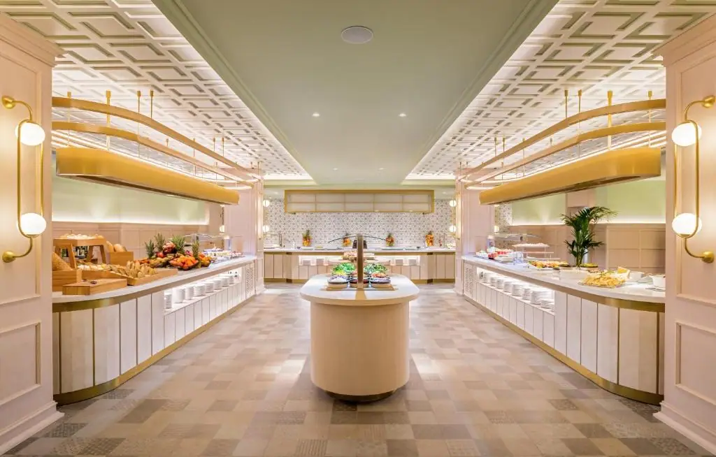 Symmetrical buffet restaurant with a central island, pale counters with gold trims and a coffered ceiling
