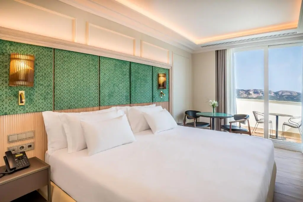 Room with a wooden headboard and green upholstered panels, and a terrace with views of the mountains
