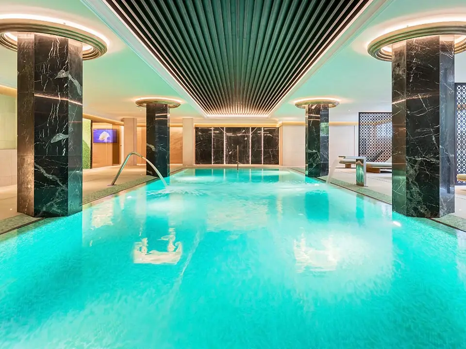 Indoor spa pool with a slatted ceiling, dark veined stone columns and turquoise mosaic