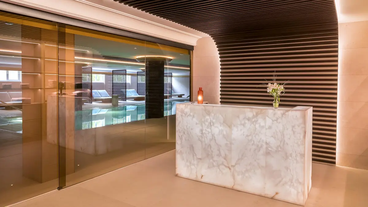 Spa reception with a backlit alabaster counter, glass enclosure and slatted wall