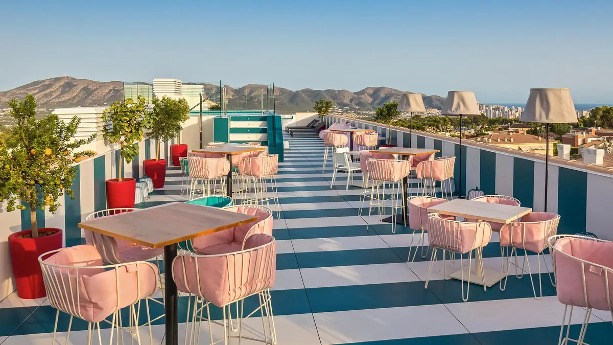 Roof terrace with a white and blue striped floor, pink chairs, lemon trees and views of the mountains and the sea