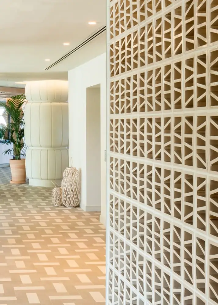 White ceramic lattice in the foreground and a plaster column in the background on herringbone flooring