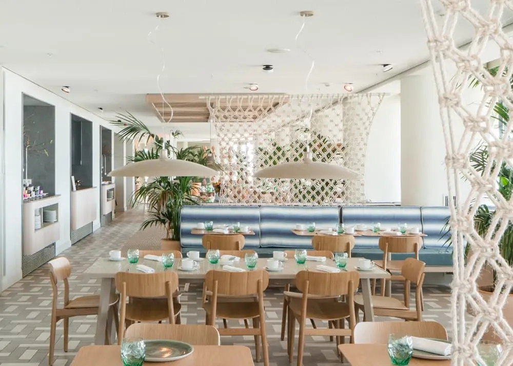 Restaurant dining room with timber tables, a striped upholstered bench and macramé screens