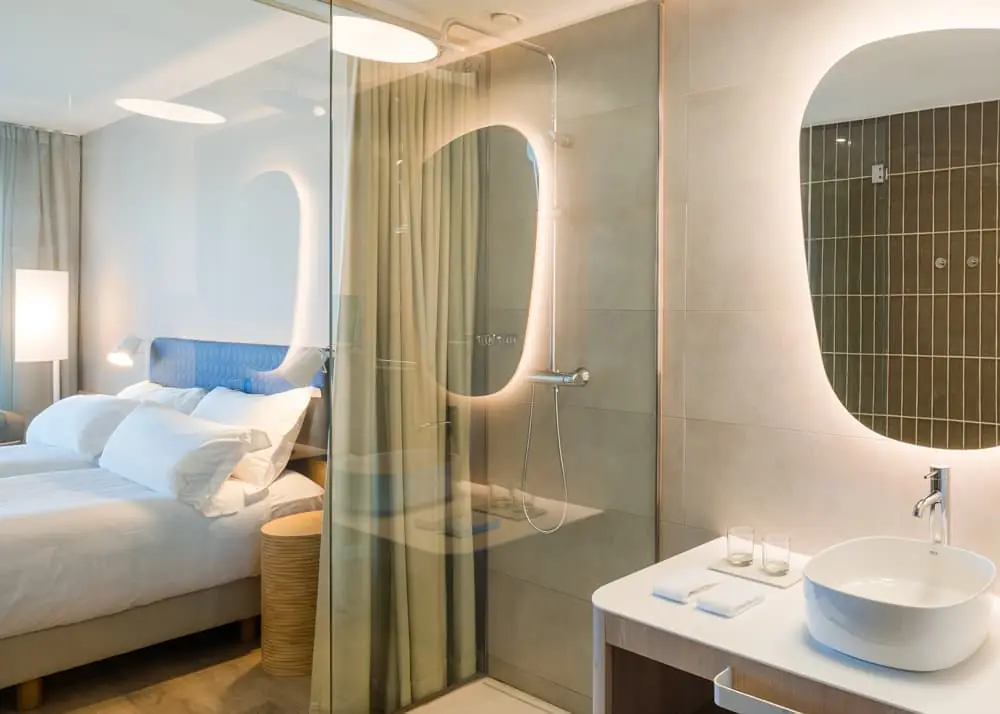 Room with a bathroom integrated behind a glass screen, a countertop washbasin and backlit mirrors