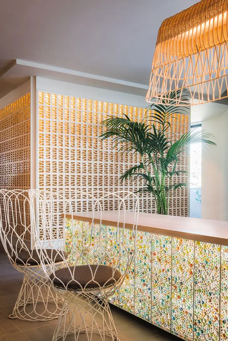Reception desk with a front of backlit coloured marbles, white wire chairs and a wicker lamp