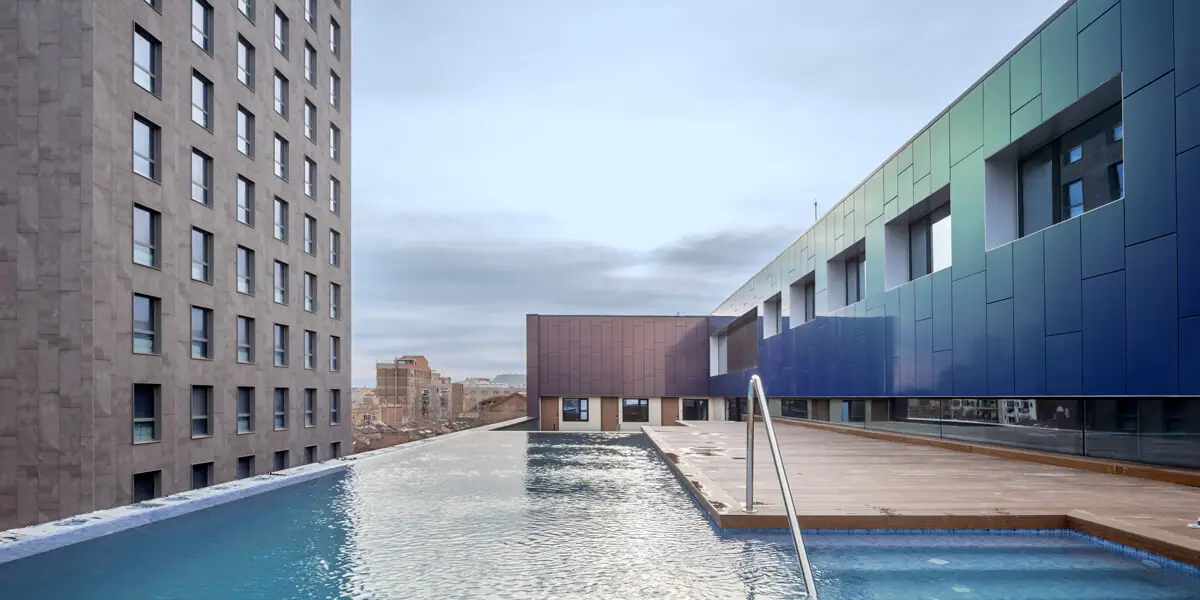 Piscina infinita en la azotea del hotel con tarima y el volumen de paneles azules y verdes al fondo