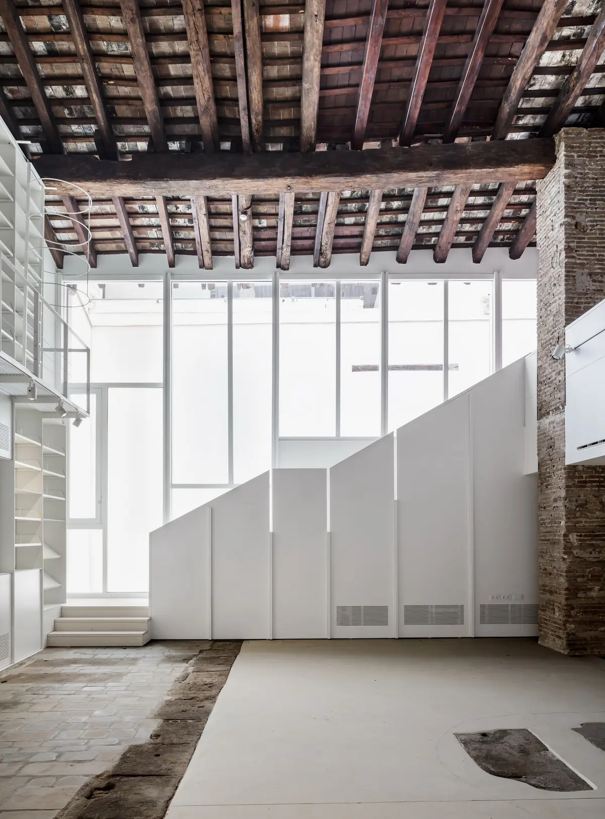 Fachada interior de vidrio de La Seca 2 bajo la cubierta de madera, con un volumen blanco escalonado delante
