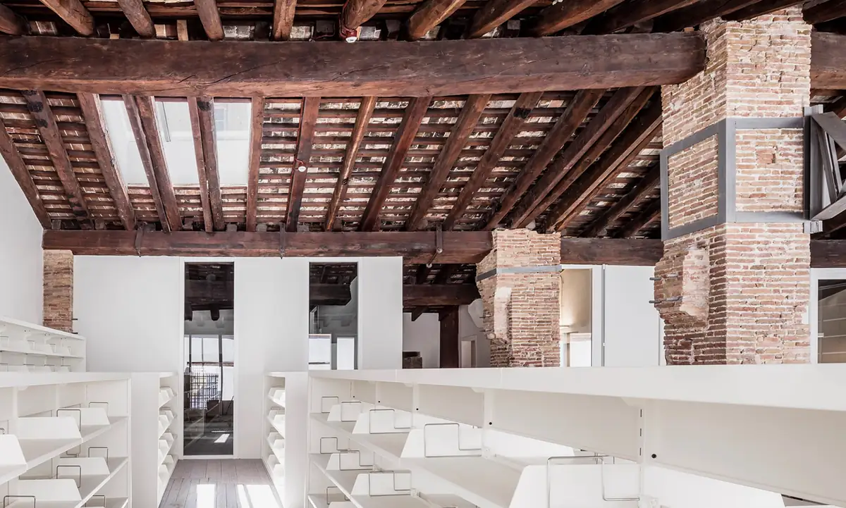 Interior de La Seca 2 con cubierta de vigas de madera, pilares de ladrillo y estanterías blancas