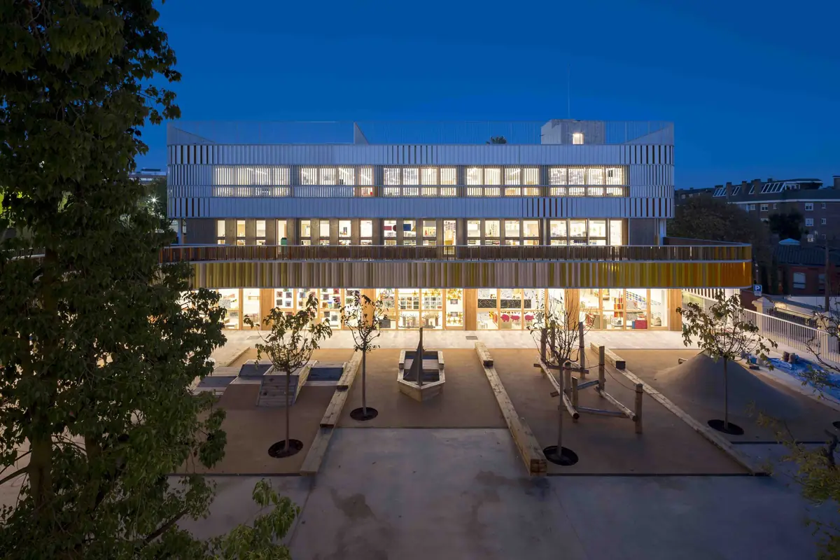 Patio central y nuevo edificio iluminado al anochecer, con las aulas encendidas tras las lamas