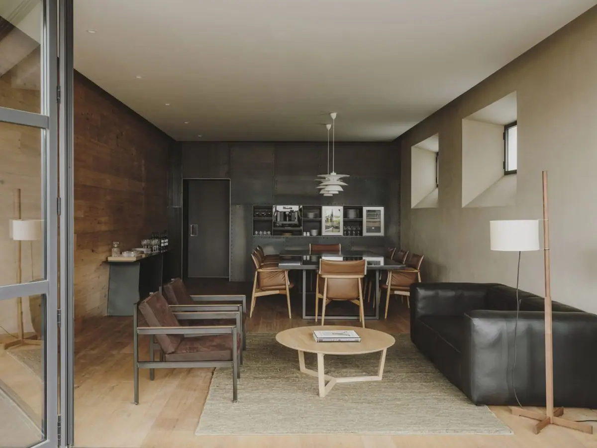Sala con mesa de comedor, sillas de madera, sofá de piel negro y una pared de chapa metálica al fondo